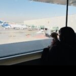 空港ターミナルの窓から、駐機中のアエロメヒコ航空の飛行機を眺めている女性とトイ・プードルの後ろ姿。日本からメキシコへのペット輸送の出発風景